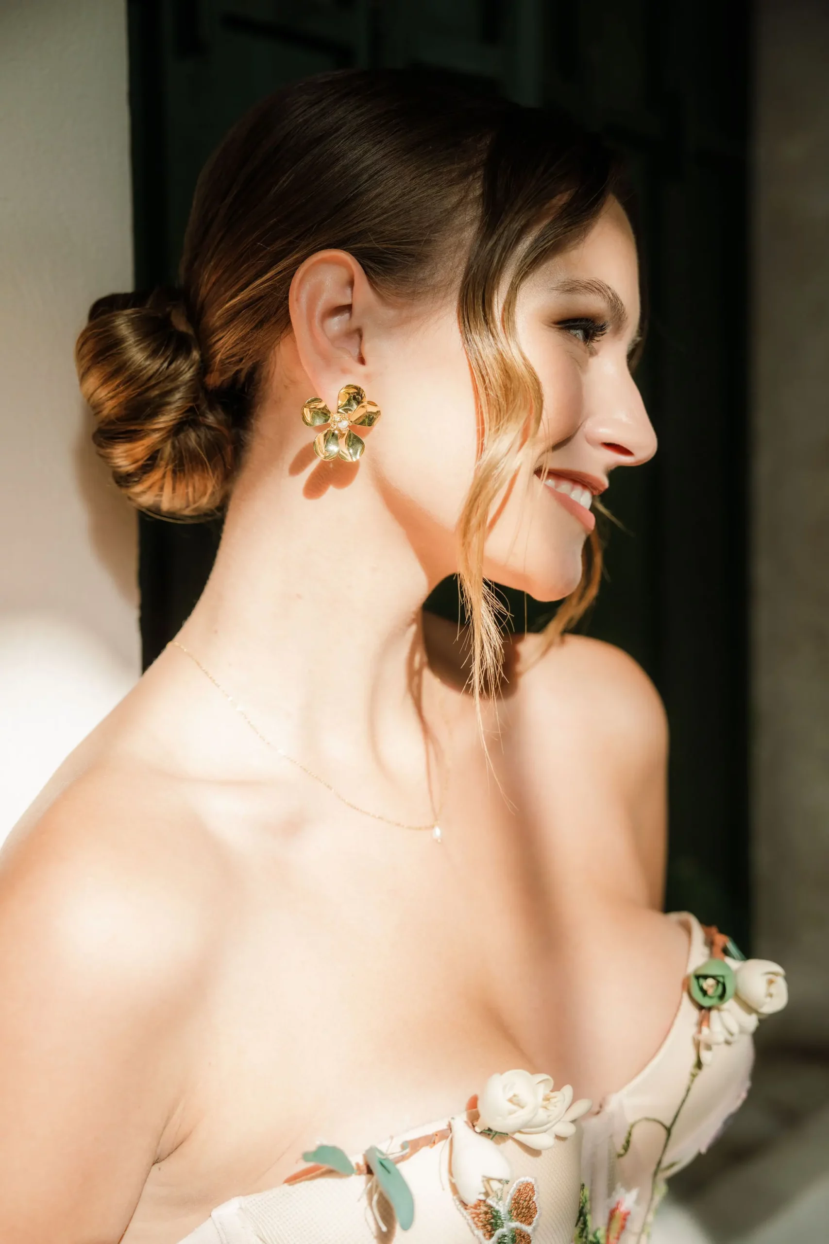 Une mariée coiffée d'un chignon bas. Elle a des mèches de cheveux bouclés qui retombent sur son visage, mais qui laissent visible son maquillage plutôt léger. Elle a un fard à paupières brun sur les yeux et un rouge à lèvres nude.