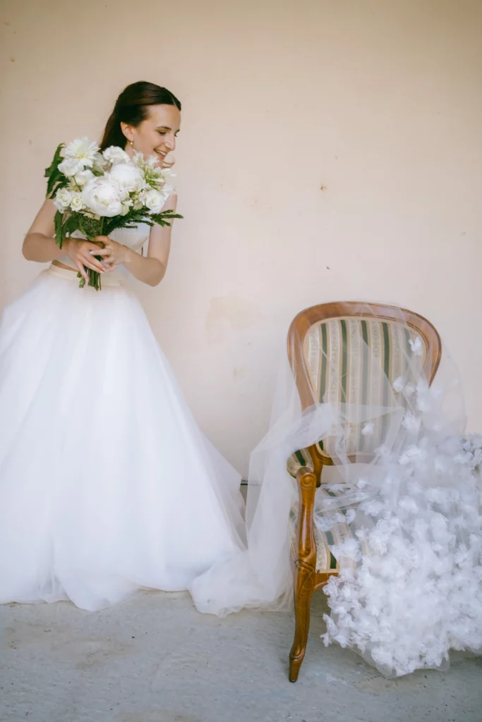 La mariée pose en robe blanche avec son voile et son beau bouquet de fleur blanche.